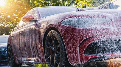Voiture rouge en cours de lavage avec un jet d'eau à haute pression.